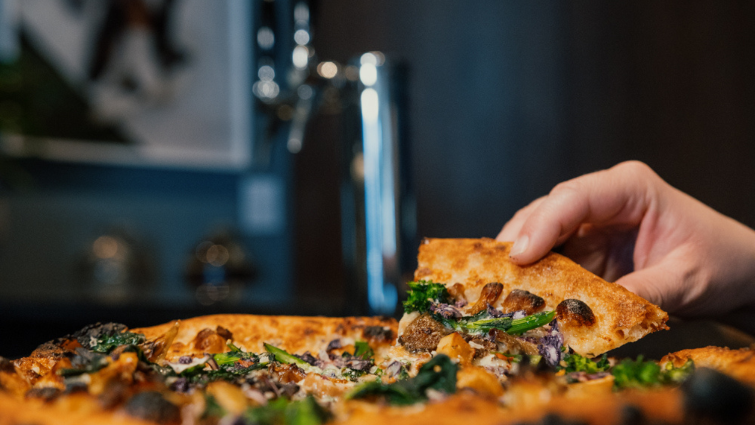 Close up of hand pulling out a slice of brick oven pizza
